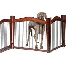 Hund hinter einem braunen, freistehenden Haustiergitter