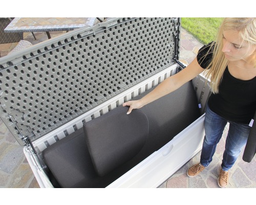 Frau räumt Kissen in eine graue und weiße Gartenbox.