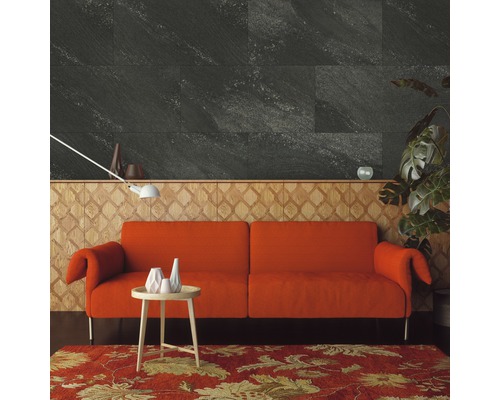 Wohnzimmer mit grauen Wandfliesen in Steinoptik, einem orangefarbenen Sofa und einem gemusterten Teppich