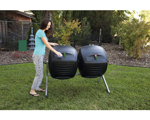 Zwei Komposttrommeln mit einer Frau, die eine der Trommeln öffnet, im Garten.