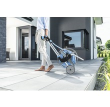 Gartenszene mit Person, die einen Schlauchwagen mit Gartenschlauch zieht.
