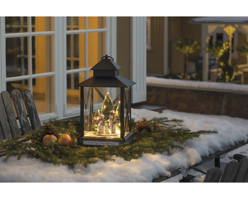 Dekorative Weihnachtslaterne mit Schneemannfiguren und Tannengrün auf einem Tisch im Freien.