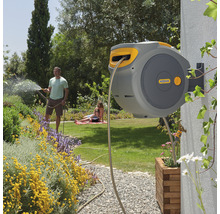 Automatische Schlauchbox an einer Hauswand mit einem Mann, der den Garten bewässert