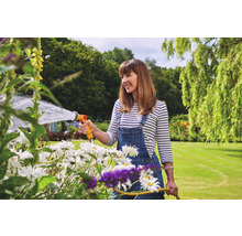 Frau gießt mit einem Gartenschlauch Blumen im Garten.