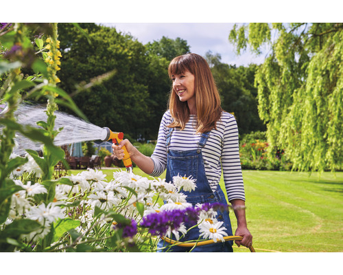 Frau gießt mit einem Gartenschlauch Blumen im Garten.