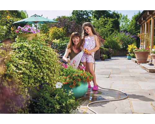 Frau und Mädchen gießen Blumen mit einem Gartenschlauch im Garten.
