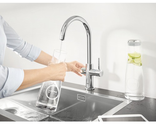 Frau befüllt ein Glas mit einer Grohe Blue Armatur in einer Spüle.