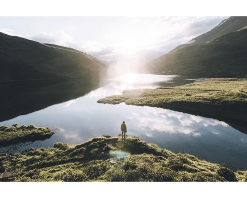 Person steht am Seeufer vor Berglandschaft