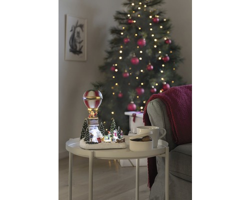 LED Szenerie Konstsmide Heißluftballon H 24 cm Zuleitungslänge 1,8 m 13 LEDs Lichtfarbe bunt Dekorative Weihnachtslandschaft mit Heißluftballon auf einem Tisch neben einem Weihnachtsbaum.