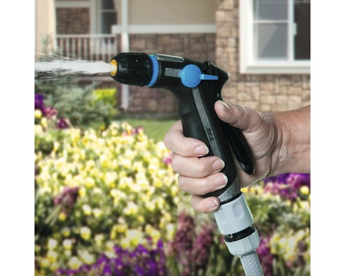 Eine Hand hält eine Gartenspritze und bewässert Pflanzen.