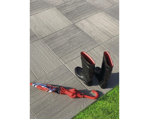 Terrassenplatten mit Holzoptik, Gummistiefel und Regenschirm auf Rasen