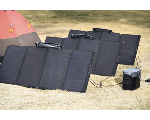 Mehrere Solarpaneele auf dem Boden mit tragbarem Kraftwerk und Zelt im Hintergrund