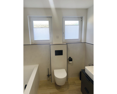 Helles Badezimmer mit Toilette, Waschbecken, Badewanne und zwei Fenstern mit Plissees