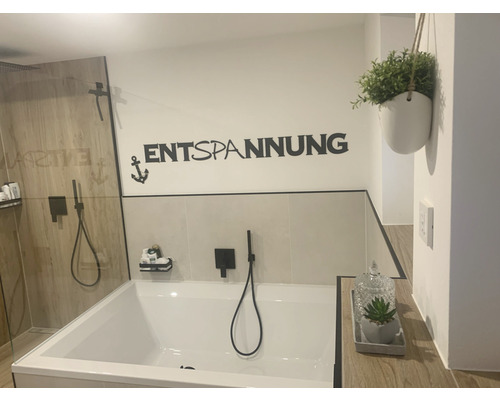 Badezimmer mit Badewanne, Dusche, Wanddekoration mit der Aufschrift Entspannung und einer Pflanze