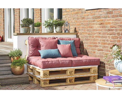 Gartenlounge aus Europaletten mit Polsterauflagen und Kissen vor einer Ziegelwand