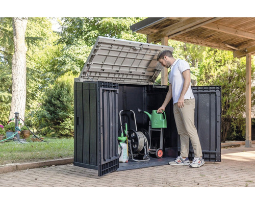 Gartenschrank mit geöffnetem Deckel und Gartengeräten sowie einer Person, die eine Gießkanne hält