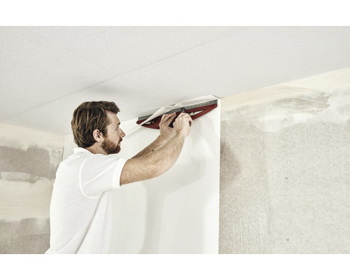 Ein Mann verwendet ein Schneidwerkzeug, um Tapeten an einer Wand anzubringen.