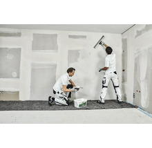 Zwei Handwerker verspachteln eine Wand in einem Innenraum.