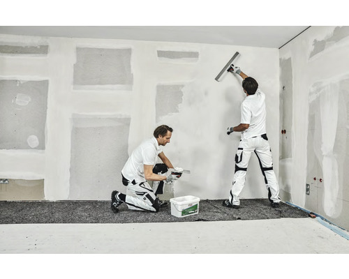 Zwei Handwerker verspachteln eine Wand in einem Innenraum.