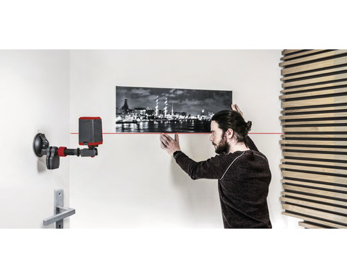 Mann richtet Bild mit Laser-Wasserwaage an der Wand aus.