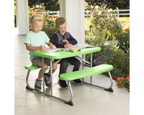 Zwei Kinder sitzen an einem grünen Picknicktisch im Freien und malen.
