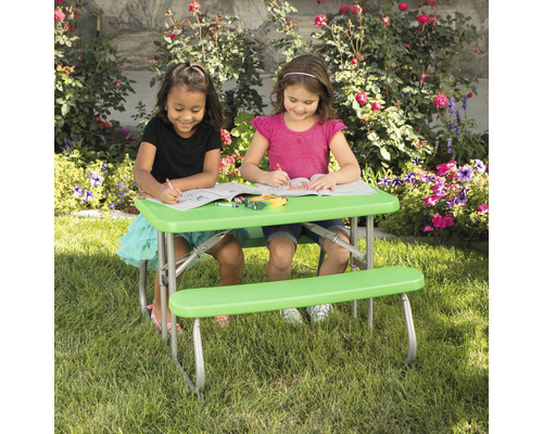 Zwei Kinder sitzen an einem grünen Kindertisch mit Bänken im Garten und malen.