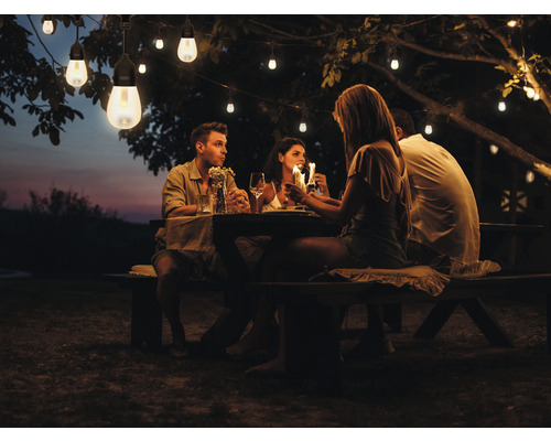 Gruppe von Personen sitzt an einem Tisch unter einer Lichterkette im Garten.