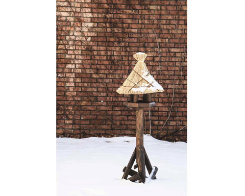 Vogelhaus aus Holz mit Strohdach im verschneiten Garten