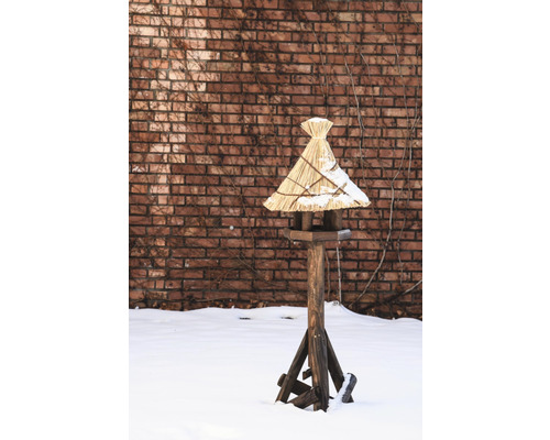 Vogelhaus mit Strohdach auf einem Holzständer im Schnee