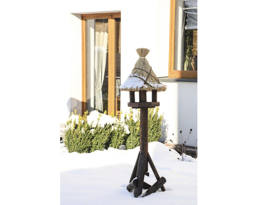 Vogelhaus aus Holz mit Strohdach im winterlichen Garten.