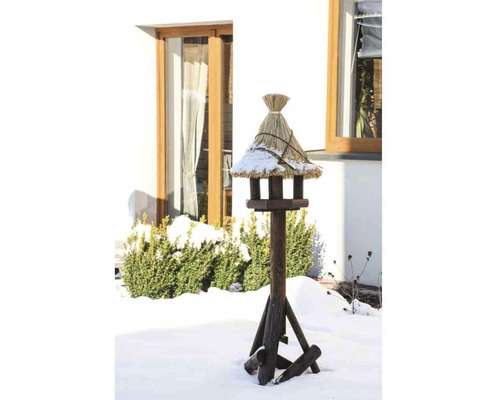 Vogelhaus mit Strohdach auf einem Holzständer im verschneiten Garten.