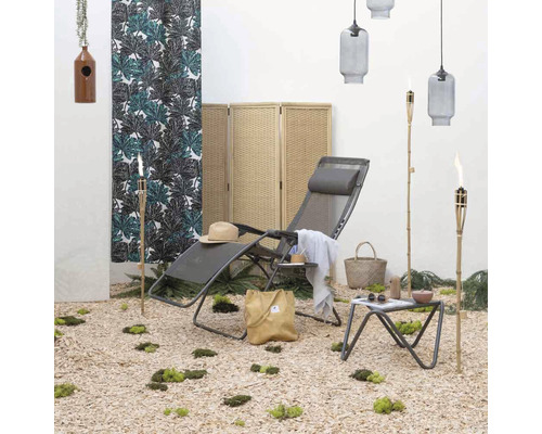 Szene mit Gartenliege, Tisch, Fackel, Hocker, Raumteiler und dekorativen Elementen für den Außenbereich.