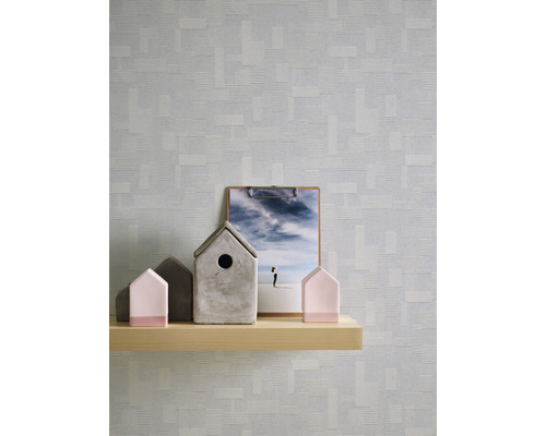 Szene mit einer Holzablage, auf der dekorative Häuser und ein Klemmbrett vor einer gemusterten Tapete stehen.