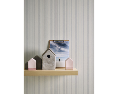 Dekorative Häuser und ein Klemmbrett auf einem Holzregal vor einer gestreiften Tapete