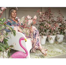 Dekorativer Außenbereich mit Frau auf Bank, Flamingoskulptur und Pflanzen in Töpfen.