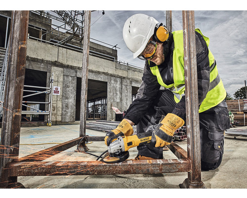 Ein Arbeiter schleift Metall mit einer Flex auf einer Baustelle, während er Schutzausrüstung wie Helm, Schutzbrille, Gehörschutz und Handschuhe trägt.
