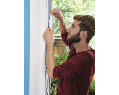 Mann befestigt Dichtungsband an einem Fensterrahmen.