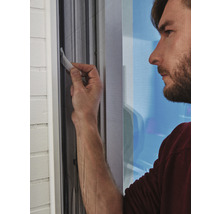 Ein Mann befestigt ein Insektenschutzgitter an einem Fensterrahmen.