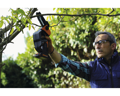 Eine Person benutzt eine Akku-Kettensäge zum Beschneiden eines Baumes.