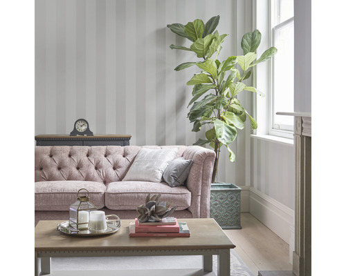 Wohnzimmer mit gestreifter Tapete, Sofa, Tisch und Zimmerpflanze.