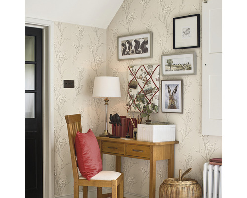 Eckansicht eines Raumes mit Schreibtisch, Stuhl und dekorativen Bildern an der Wand, tapeziert mit einem Muster aus kleinen Blüten und Zweigen.