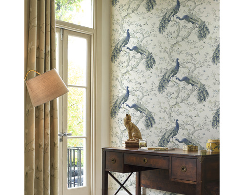 Ein Arbeitszimmer mit einem Schreibtisch aus Holz, einer Lampe und einer Wandtapete mit Pfauenmuster.