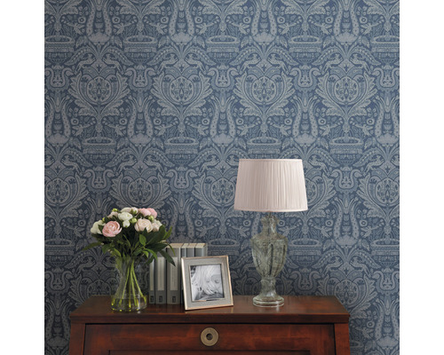 Dekorative Tapete mit Muster auf einer Zimmerwand, Tisch mit Lampe, Blumen und Bilderrahmen