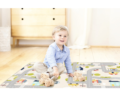 Kind spielt mit Holzautos auf einem Spielteppich mit Straßenmotiv.