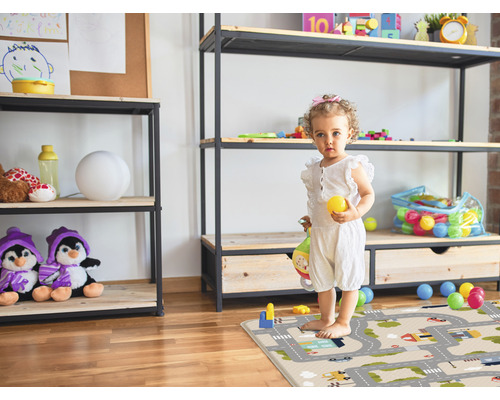 Kind steht auf einem Spielteppich in einem Kinderzimmer mit Regalen und Spielzeug.