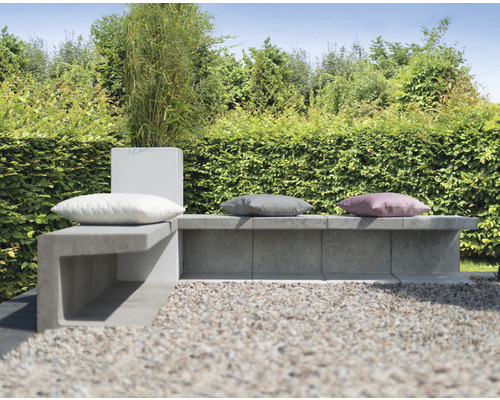 Gartenmöbel-Sitzgruppe mit Betonbank und Kissen vor grüner Hecke