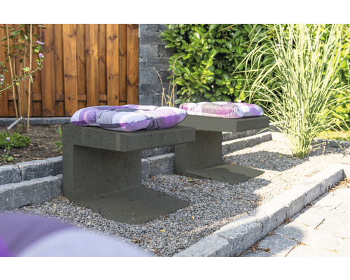 Zwei graue Gartenbänke aus Beton mit Sitzkissen im Außenbereich.