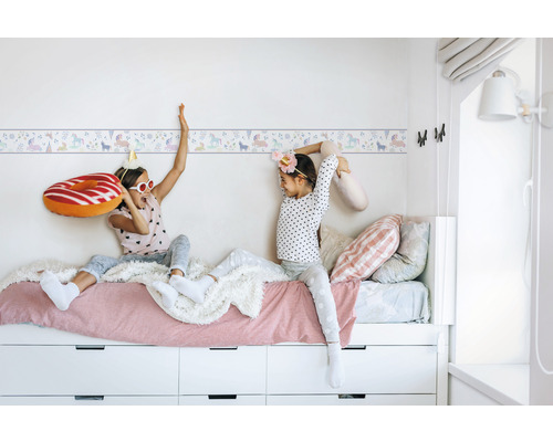 Kinderzimmer mit Einhorn Bordüre und spielenden Kindern auf einem Bett mit Schubladen
