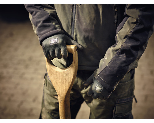 Eine Person in Arbeitskleidung hält einen Spaten mit Holzgriff und trägt Arbeitshandschuhe.