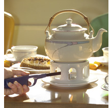 Teekanne auf einem Tisch mit Kuchen und einer Person, die ein Teelicht anzündet